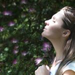 Breathing - Woman Closing Her Eyes Against Sun Light Standing Near Purple Petaled Flower Plant