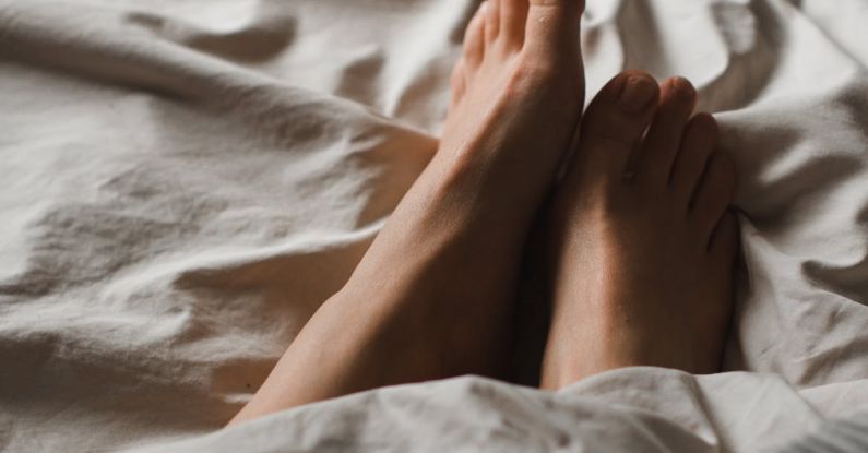 Naps - Crop anonymous barefoot female feet relaxing on soft comfy bed under white warm blanket in dark bedroom