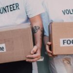 Causes - Man and Woman Carrying Medicine and Food Labelled Cardboard Boxes Behind a White Van