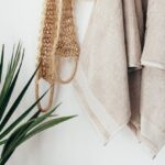 Routine - Stylish bathroom interior with houseplant on wooden table against white wall with hanging towels and set of eco friendly body care items