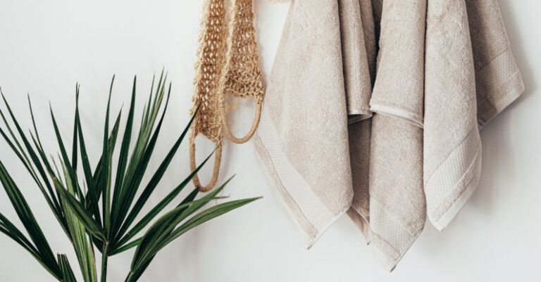 Routine - Stylish bathroom interior with houseplant on wooden table against white wall with hanging towels and set of eco friendly body care items