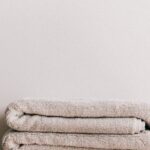 Routine - Minimalist composition of white simple stool with clean fresh folded gray towels against beige wall in bathroom