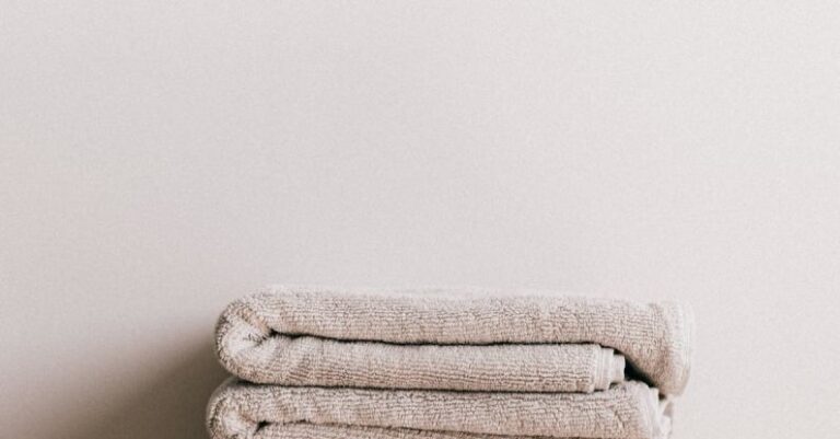 Routine - Minimalist composition of white simple stool with clean fresh folded gray towels against beige wall in bathroom