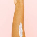 Therapy - Female arm with smear for skin care against pink background