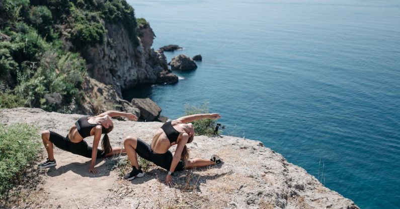 Exercises - Women in Black Shorts and Sports Bra Bending their Body Near the Cliff